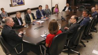 Fotografia da sala de reuniões da presidência. Ao centro mesa de reunião,. no entrono 14 pessoas. 