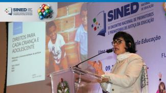 Imagem mostra representante do Unicef em primeiro plano falando ao microfone. Ao fundo, projeção sobre dados informados pela palestrante e a logo do evento.