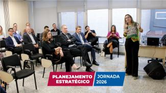 Imagem da apresentação da Apla aos representantes do TCE/SC. Em uma sala, há homens e mulheres sentados em cadeiras, de frente para a assessora Adriana Luz, que fala ao microfone sobre as ações desenvolvidas pela Apla. À frente da foto, embaixo, há os títulos “Planejamento Estratégico” e “Jornada 2026”, destacados sobre retângulos vermelho e azul, respectivamente.