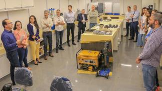 Foto da visita realizada pelos assessores de conselheiros ao laboratório de obras rodoviárias do TCE/SC. Há homens e mulheres, em pé, um ao lado do outro, em formato de U, ao redor de uma bancada com diversos equipamentos. Entre eles, estão Rodrigo Luz Glória, chefe da Divisão do Laboratório de Obras Rodoviárias, e Sidney Tavares Júnior, diretor-geral de Controle Externo da instituição. 