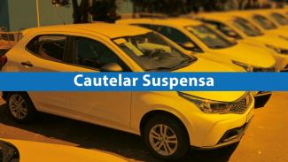 Imagem de uma fileira de carros compactos estacionados, todos na cor branca, vistos em um pátio ao ar livre. Sobre o carro em primeiro plano há uma faixa horizontal azul com o texto em branco “Cautelar Suspensa” 