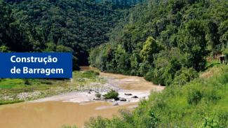 Banner horizontal com imagem de uma barragem em área natural, formada por um curso de água represado com águas barrentas, cercado por vegetação densa e verde. À esquerda da imagem, há um retângulo azul com o texto “Construção de Barragem”.