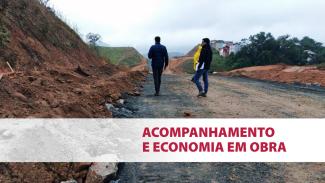 Imagem mostra uma rodovia em processo de abertura, com um barranco de terra à esquerda. Ao centro, duas pessoas vestindo roupas escuras (uma delas com uma prancheta na mão) vistoriam o local