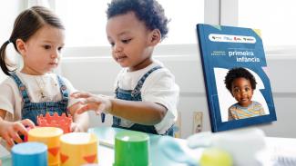Banner horizontal com fundo claro mostrando, à esquerda, duas crianças pequenas brincando em uma mesa com brinquedos coloridos. Uma menina de cabelos escuros presos e um menino de cabelos cacheados vestem roupas casuais e interagem com peças lúdicas, em um ambiente iluminado que remete à educação infantil. À direita, aparece a imagem de uma publicação intitulada “Sumário Executivo — primeira infância”, cuja capa exibe a foto de uma criança e logos institucionais na parte superior.