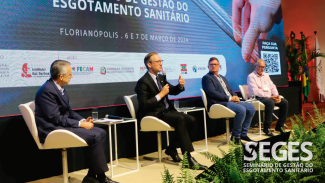 Foto dos quatro participantes do painel durante o Seminário. Da esquerda para a direita, o presidente da Agir, Mário Hildebrandt, o desembargador do TJSC Marcos Fey Probst, o presidente da Aresc, João Carlos Grando, e o presidente, em 2023, do Conselho de Administração da Aris, Mario Afonso Woitexem. Ambos estão sentados em poltronas, no palco do auditório do evento, enquanto debatem. Ao fundo, projeção do logo do Seges no telão. 