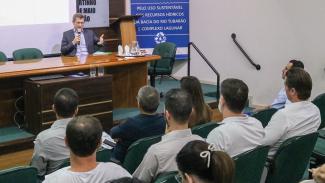 Foto do vice-presidente do TCE/SC, José Nei Ascari, sentado, em uma mesa que serve de tribuna, palestrando. À sua frente aparecem sentados em cadeiras do auditório, os participantes da reunião. 