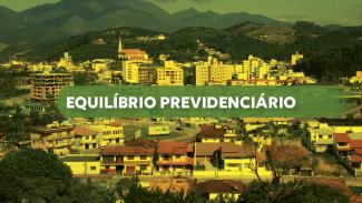 Banner horizontal com foto, com filtro amarelado, de uma vista panorâmica de uma cidade com casas e prédios, cercada por morros e montanhas ao fundo. No centro da imagem há uma faixa verde translúcida com o texto “Equilíbrio previdenciário”. 