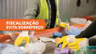 Banner horizontal com foto de resíduos sólidos (lixo) sendo selecionados em uma esteira. Os trabalhadores vestem uniforme e luvas durante a separação. Sobre a foto, em tarja laranja, o texto "Fiscalização evita sobrepreço". 