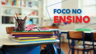 Banner horizontal com foto de materiais escolares empilhados sobre cadernos em uma mesa. Há um porta-lápis e óculos de grau, cadernos e livros. Sobre a foto, o texto "Foco no ensino", em fonte colorida.