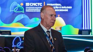 Foto do presidente do TCE/SC, conselheiro Herneus De Nadal, no III Congresso Naciional de Comunicação dos Tribunais de Contas. Eles estpa de terno escuro. Ao fundo, um painel em tons de azul e verso com a logo do evento,