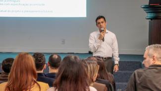 Banner horizontal com foto do diretor da DTI, Rafael Queiroz, falando ao microfone em pé, no auditório do TCE. Na frente dele, de costas e em primeiro plano na foto, várias pessoas sentadas em poltronas na plateia. Ao fundo, projeção de slides no telão.