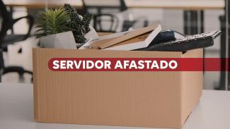 Imagem mostra uma caixa de papelão sobre uma mesa de escritório. No centro, escrito em branco sobre tarja vermelha, está escrito Servidor Afastado
