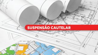 Imagem mostra projetos de arquitetura e engenharia sobre uma mesa. Do centro para a direita, sobre uma tarja vermelha, está escrito "suspensão cautelar" em letras brancas