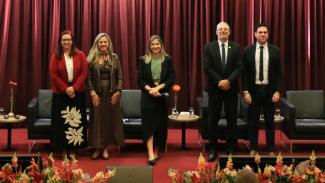 Banner horizontal com foto posada dos cinco palestrantes no palco do auditório bordô do TCE/SC. Entre os presentes, o conselheiro substituto Gerson Sicca, a diretora executiva do Icon, Marina de Miranda, a advogada Caroline Bitencourt, a presidente do IPDA, Adriana Schier, e o procurador Janriê Reck. Eles estão em pé. O cenário é composto por tapete e cortinas bordôs, além de flores decorativas. 