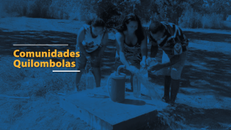 Foto horizontal com filtro azul de três pessoas reunidas ao redor de uma estrutura simples de abastecimento de água ao ar livre. As três estão inclinadas para frente, lavando as mãos ou enchendo recipientes em um ponto de água que sai de um cano. À esquerda da imagem, aparece o texto “Comunidades Quilombolas” em amarelo.