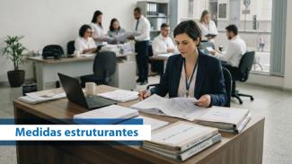 Banner horizontal com foto de uma mulher em escritório. Ao fundo, outras pessoas trabalhando. Sobre a foto, o texto “Medidas estruturantes”. 