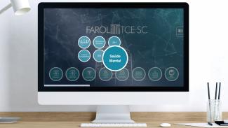 Imagem mostra uma tela de computador sobre uma mesa. Na tela, com fundo azul escuro, há uma página que remete ao Farol, ferramente de dados do TCE/SC. Há uma série de botões arredondados, e um deles, à direita, está em destaque com a expressão “saúde mental”