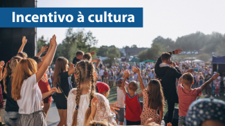 Banner horizontal com foto de várias pessoas apresentando um show, no palco. Elas erguem os braços. À frente, há pessoas que assistem, em local aberto. Sobre a foto, no canto superior esquerdo, em tarja azul, o texto “Incentivo à cultura”, em fonte branca.