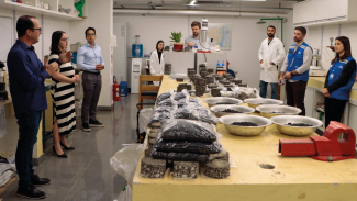 Banner horizontal com foto que mostra equipe do TCE/SC reunida juntamente com a comitiva do Cincatarina. Eles estão no laboratório. Na mesa, ao centro, há vários materiais e equipamentos de obras de pavimentação asfáltica. Entre os presentes a coordenadora Renata Ligocki Pedro e o chefe da divisão, Rodrigo Glória.