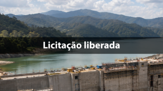 Vista panorâmica de uma barragem em construção, com estrutura de concreto em primeiro plano, reservatório de água ao centro e montanhas cobertas por vegetação ao fundo. Sobre a imagem, aparece o texto: “Licitação liberada”.