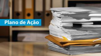 Pilha de papéis e pastas com a frase “Plano de Ação” em destaque sobre fundo de arquivos.