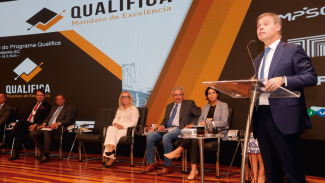 Banner horizontal com foto do ministro do STF, André Mendonça, palestrando no pulpito do auditório da Alesc. Ao fundo, sete pessoas sentadas, uma ao lado da outra, entre elas, o conselheiro Aderson Flores. Ao fundo, no telão, projeção do logo do Qualifica. 