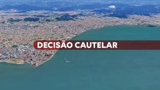Banner horizontal. Imagem aérea da Aveninda Beira-mar de São José. Sob uma tarja vermelha, está escrito em letras brancas a expressão "Decisão Cautelar".tal. Nela, uma maca vazia à esquerda. Ao centro, de costas, dois enfermeiros caminham em direção à uma porta de vidro. No canto inferior direito, sobre um fundo verde claro, em letras brancas está escrita a palavra cautelar.