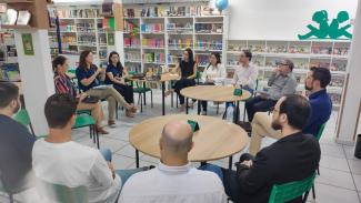 Foto do grupo durante uma reunião em uma sala com várias estantes de livros ao fundo. Os participantes estão sentados um ao lado do outro, em um círculo. Entre os presentes, os servidores do TCE/SC e membros da educação de Joinville. 
